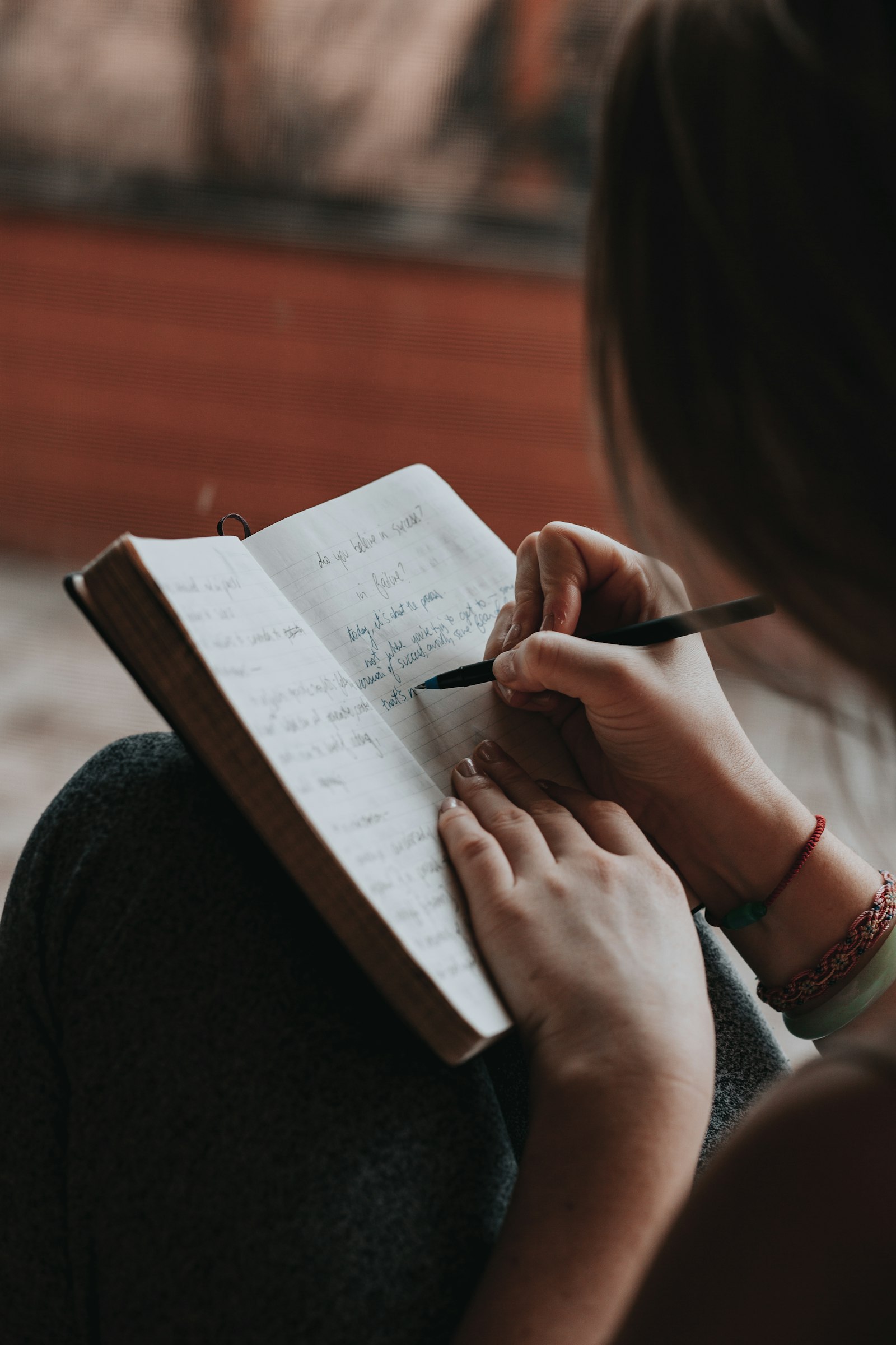 A person journaling by hand, pen in hand, warm rust-toned light.